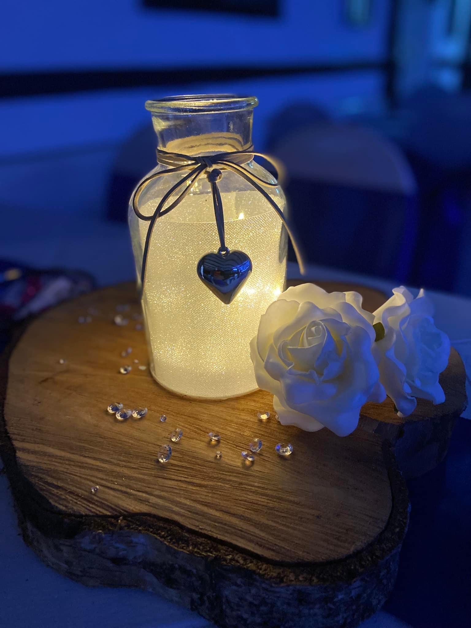 Lit jar with roses on wooden slab.