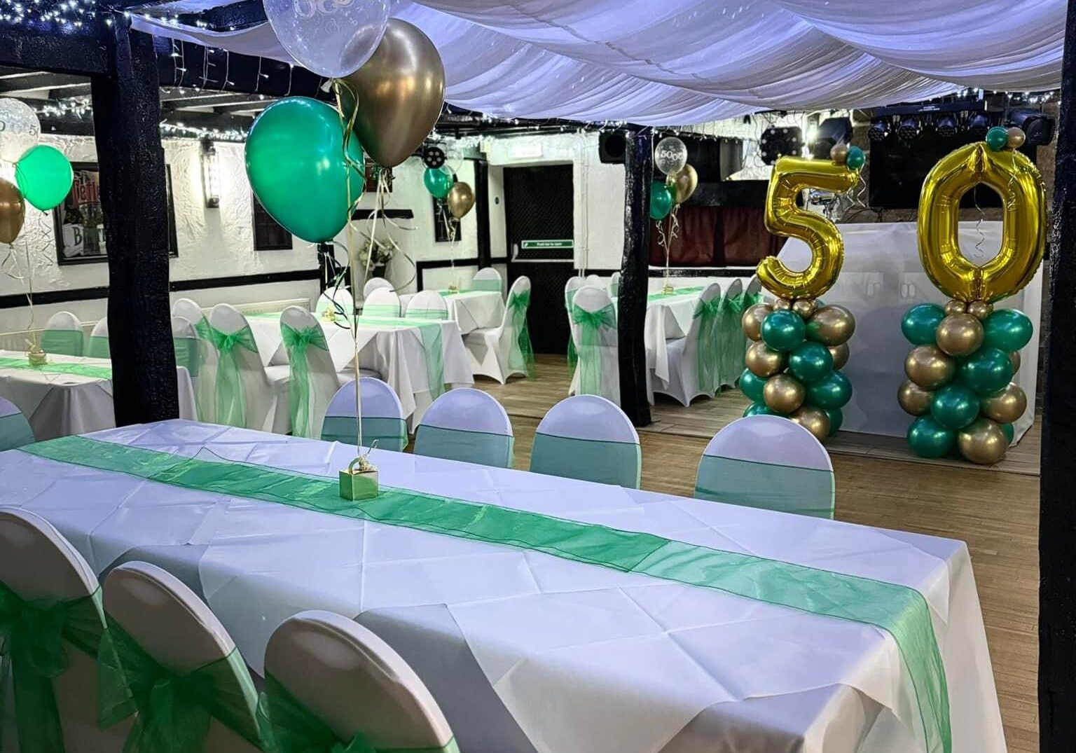 Decorated event hall with green and gold balloons.